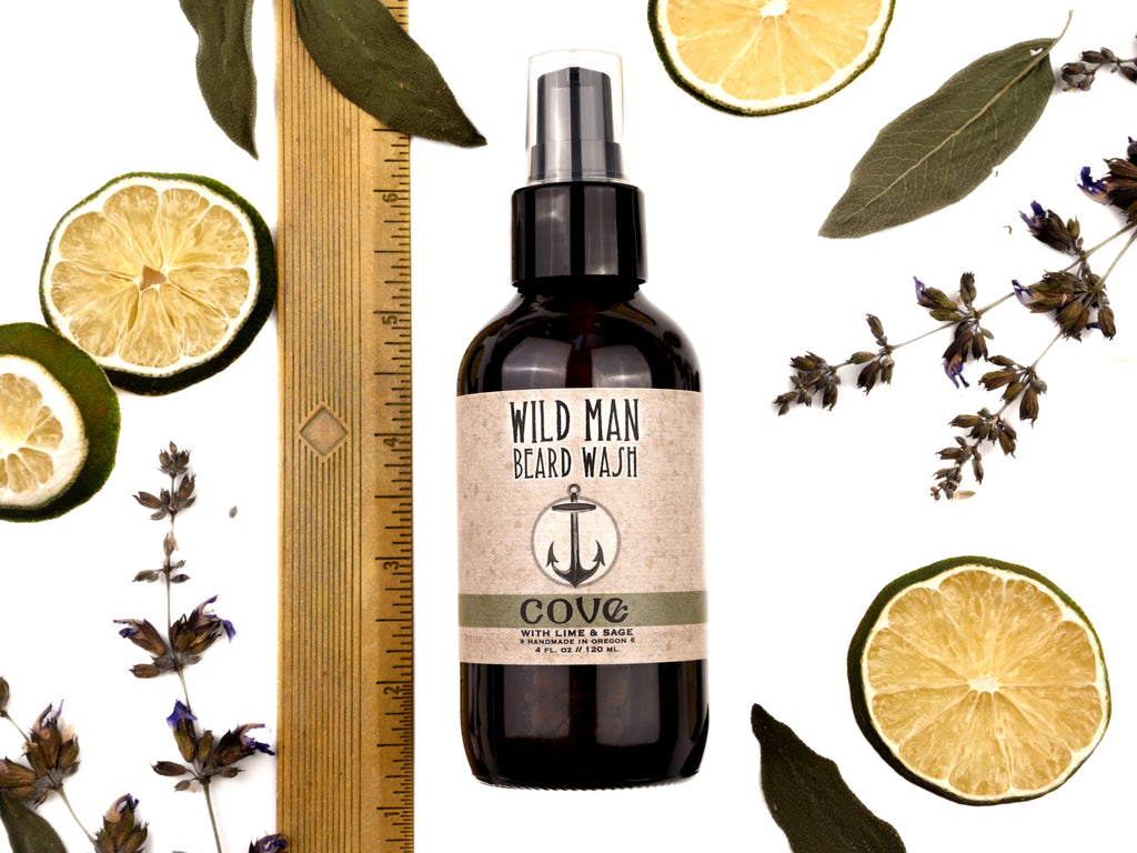 Wild Man Beard Wash Cove scent in 4oz amber bottle. Shown with ruler at about 6" tall. Lime slices and sage leaves surround.