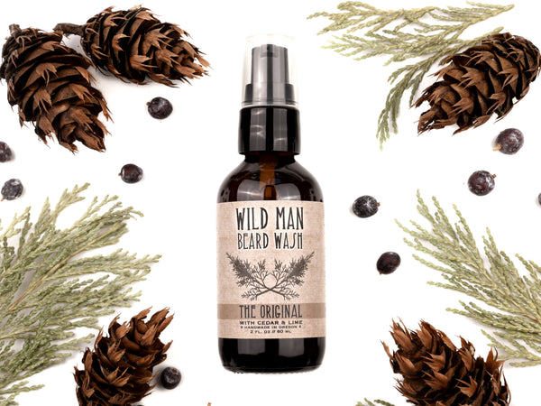 Wild Man Beard Wash in The Original scent shown in a 2oz amber glass bottle. Cedar, fir cones and juniper berries surround.