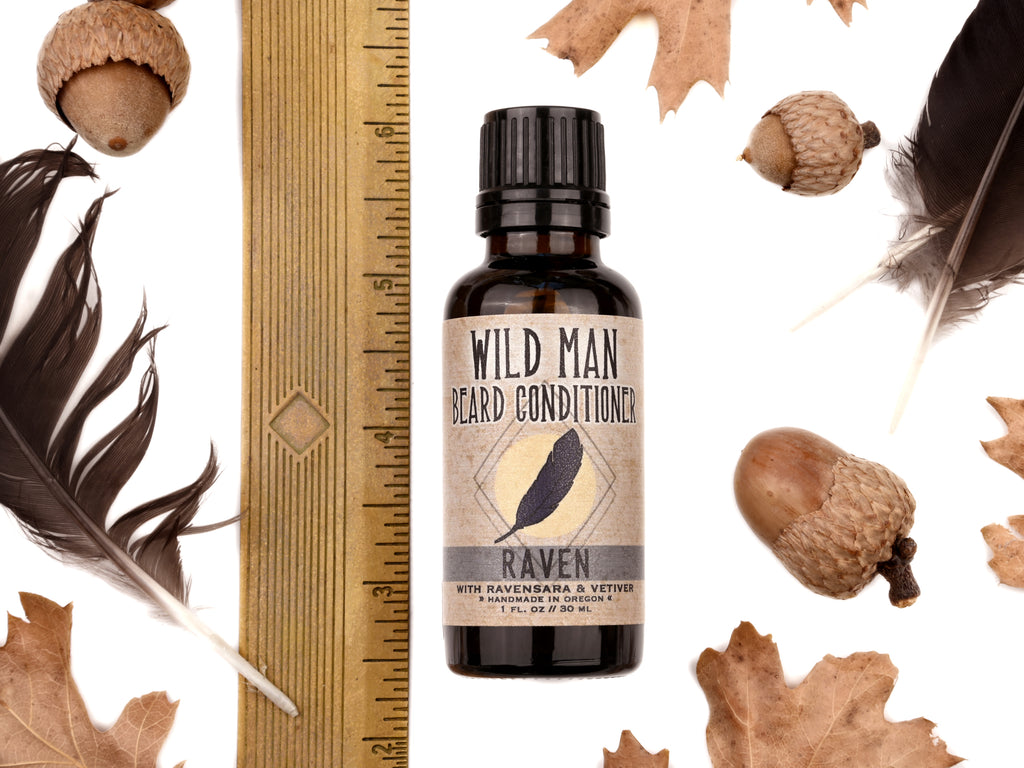Wild Man Beard Oil Conditioner - Raven scent in 30ml amber glass bottle. Shown next to ruler at about 3.75" tall. Black feathers, acorns and dried oak leaves surround. 