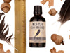 Wild Man Beard Oil Conditioner - Raven scent in 50ml amber glass bottle. Shown next to ruler at about 4" tall. Black feathers, acorns and dried oak leaves surround. 