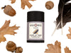 Raven Dry Shampoo in biodegradable paper shaker tube with autumnal oak leaves, acorns and black feathers surrounding.