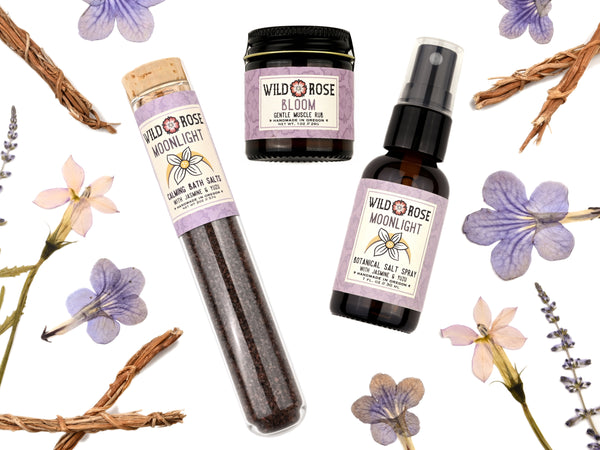 Moonlight Bath Salts, Salt Spray and Bloom Muscle Rub from Wild Rose. Dried fowers and herbs surround.