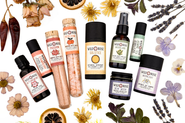 A collection of Wild Rose botanical skincare products arranged in rainbow order. Dried botanicals surround.