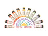 Eleven biodegradable lip balm tubes arranged in a semi-circle on a white background, with a central text graphic reading 'Biodegradable Cruelty Free Non-GMO 100% Natural.' The balm tubes show various colors including pink, orange, yellow, green, purple, and white, with Wild Rose branding visible on the labels.