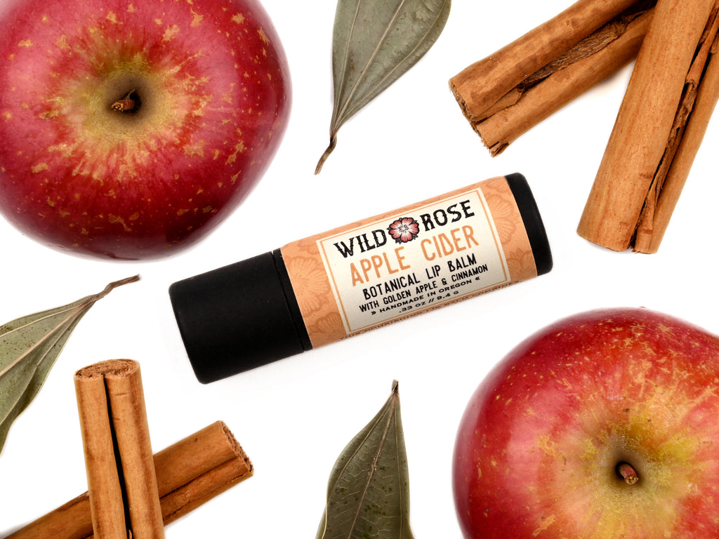 Apple Cider Natural Lip Balm in a biodegradable paper tube. Apples and cinamon sticks surround.