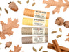 Wild Rose Autumn Lip Balm Set with Apple Cider, Banana Bread, Spiced Chai and Dark Roast Lip Balms in biodegradable tubes. Shown with dried oak leaves, acorn, cardamom pods and cinnamon sticks on a white background.
