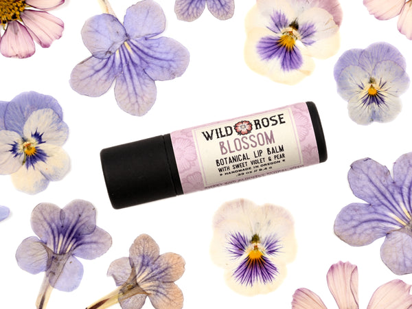 Blossom Lip Balm in a biodegradable paper tube. Pressed flowers surround.