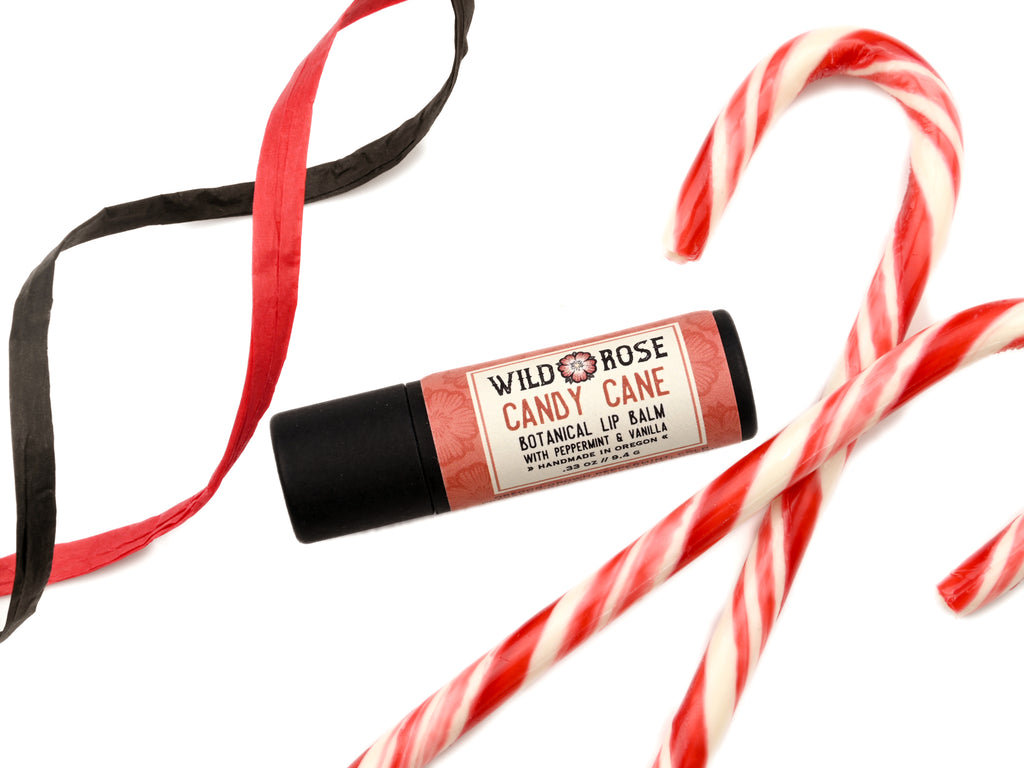 Candy Cane Natural Lip Balm in a biodegradable paper tube. Candy canes and ribbon surround.