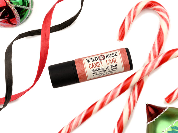 Candy Cane Natural Lip Balm in a biodegradable paper tube. Candy canes, ornaments and ribbon surround.