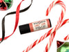 Candy Cane Natural Lip Balm in a biodegradable paper tube. Candy canes, ribbon and ornaments surround.
