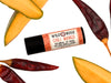 Chili Mango Natural Lip Balm in a biodegradable tube. Mango slices and dried chiles surround.