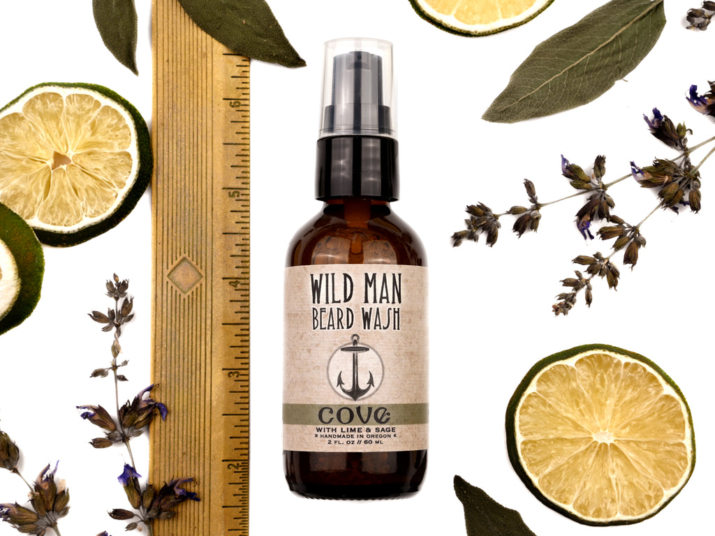Wild Man Beard Wash Cove scent in 2oz amber bottle. Shown with ruler at about 5" tall. Lime slices and sage leaves surround.
