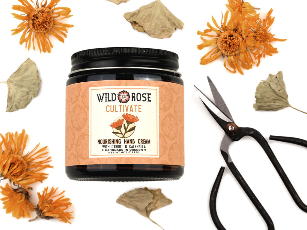 Cultivate Nourishing Hand Cream in a 4oz amber glass jar with metal lid. Shown next to tiny pruning scissors.  Dried calendula and gotu kola surround.