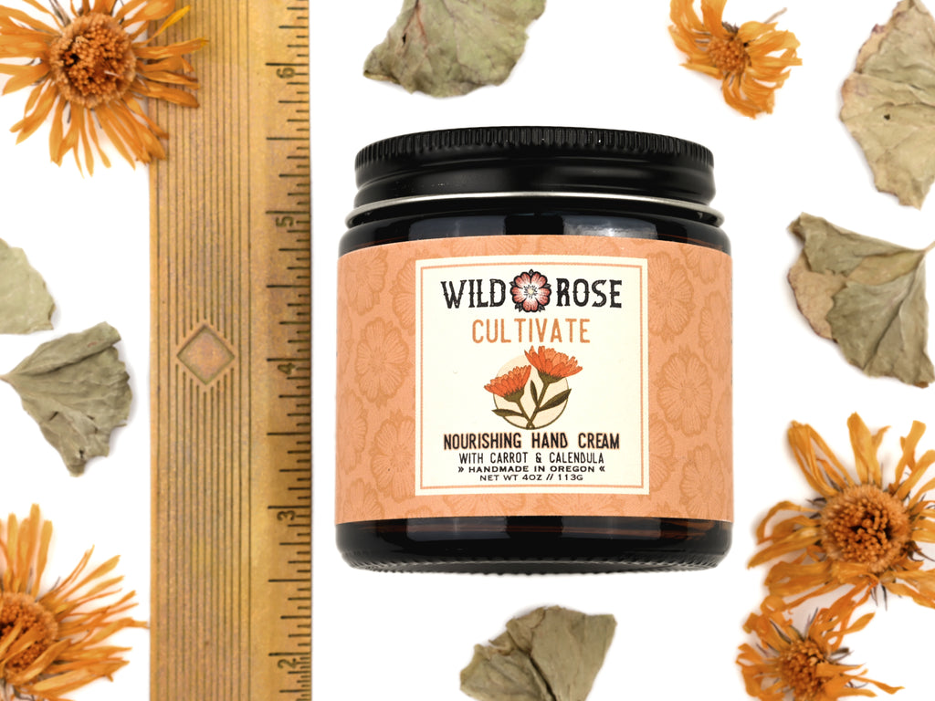 Cultivate Nourishing Hand Cream in a 4oz amber glass jar with metal lid. Shown next to ruler at about 3" tall. Dried calendula and gotu kola surround.