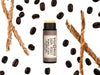 Dark Roast Lip Balm in a biodegradable tube. The cap is removed revealing a creamy lip balm.  Coffee beans and vetiver root surround.