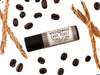 Dark Roast Lip Balm in a biodegradable tube. Coffee beans and vetiver root surround.