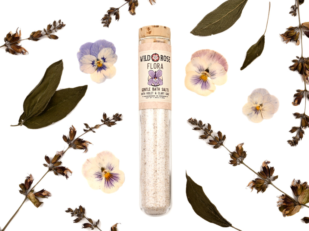 Flora Gentle Bath Salts in a glass test tube. Dried pansies and sage leaves surround.