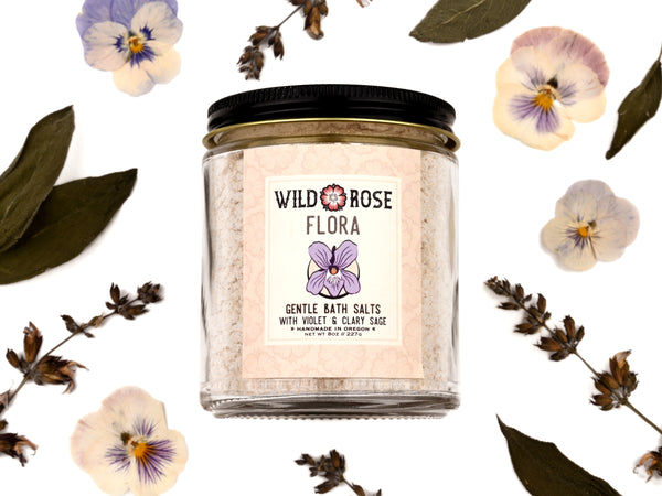 Flora Gentle Bath Salts in a glass jar. Dried pansies and sage leaves surround.