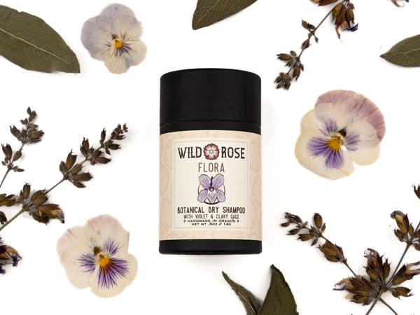 Flora Dry Shampoo in biodegradable paper shaker tube with clary sage, pressed viola flowers and sage leaves surrounding.