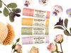Wild Rose Garden Lip Balm Set with Rosebud, Honey Bee, Basil Mint and Blossom Lip Balms in biodegradable tubes. Shown with honeycomb, dried mint, dried rosebuds and pressed pansies on a white background. 