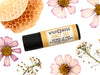 Honey Bee Natural Lip Balm in a biodegradable paper tube. Honey comb and pressed flowers surround.
