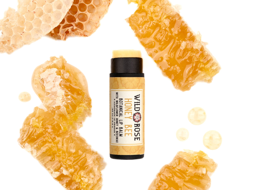Honey Bee Natural Lip Balm in a biodegradable paper tube shown with cap off revealing a creamy yellow balm. Honey comb surrounds.