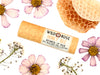Honey Bee Natural Lip Balm from Wild Rose in a biodegradable paper tube. Honey comb and pressed flowers surround.