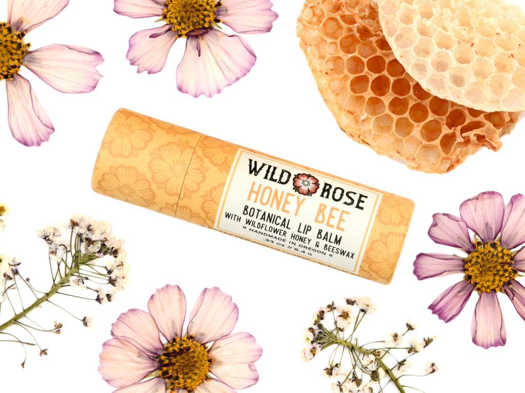 Honey Bee Natural Lip Balm from Wild Rose in a biodegradable paper tube. Honey comb and pressed flowers surround.