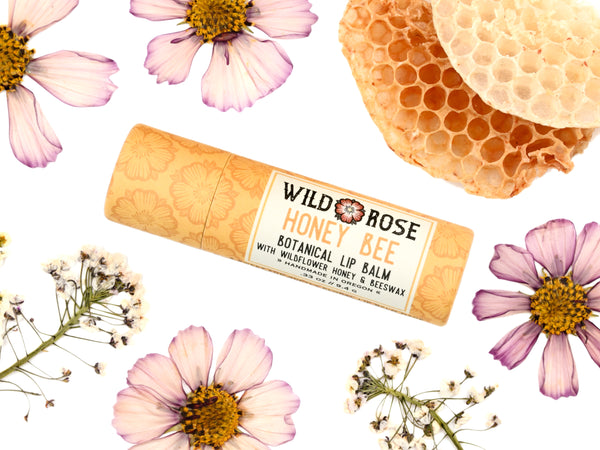 Honey Bee Natural Lip Balm from Wild Rose in a biodegradable paper tube. Honey comb and pressed flowers surround.