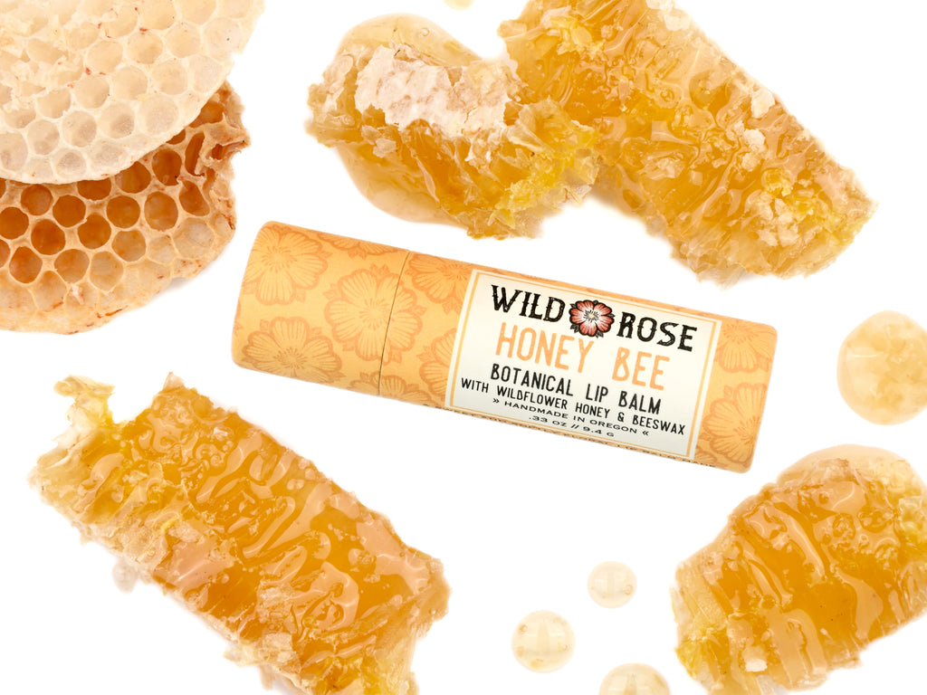 Honey Bee Natural Lip Balm from Wild Rose in a biodegradable paper tube. Honey comb pieces surround.