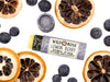 Wild Rose Lemon Berry Botanical Lip Balm in a biodegradable tube on a white background with dried lemons and blueberries surrounding. The cap is removed revealing a creamy yellow balm.
