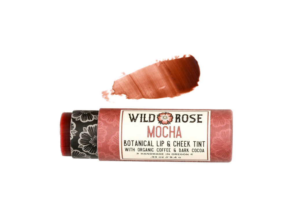 Wild Rose Mocha Botanical Lip & Cheek Tint in a biodegradable paper tube on a white background. The cap is removed and a color swatch is above, revealing a dark red tint.