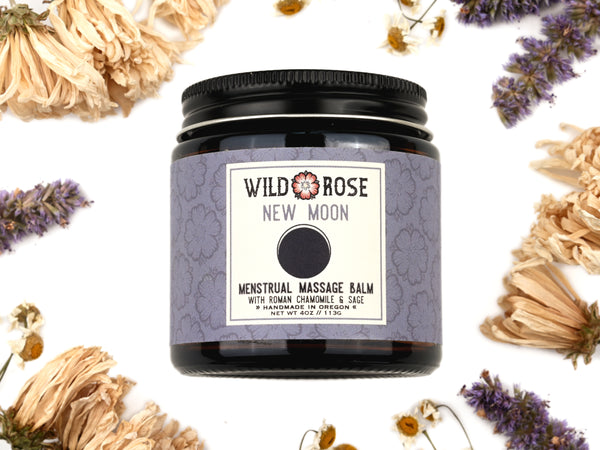 New Moon Menstrual Massage Balm in a 4oz amber glass jar with metal lid. Dried flowers surround.