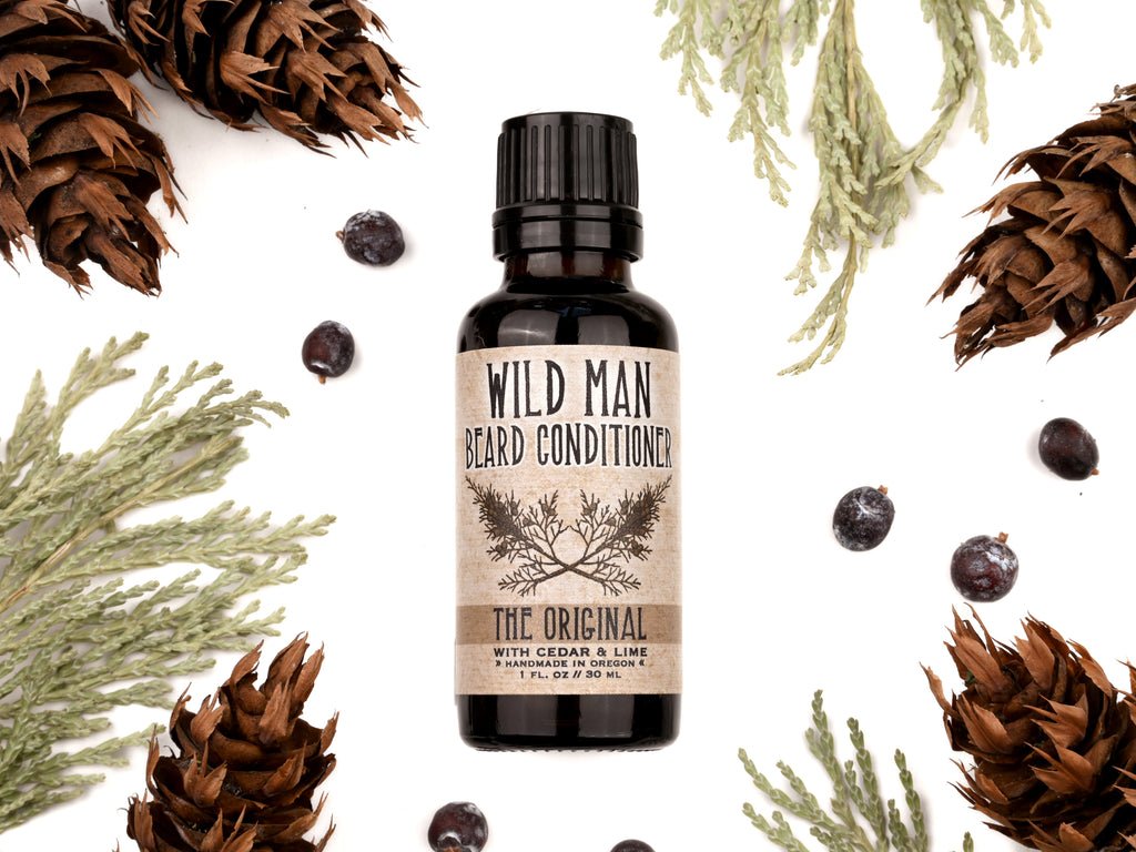 Wild Man Beard Conditioner in The Original scent shown in a 30ml amber glass bottle. Cedar, fir cones and juniper berries surround.