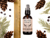 Wild Man Beard Wash in The Original scent shown in a 2oz amber glass bottle. Shown next to a ruler at about 5" tall. Cedar, fir cones and juniper berries surround.