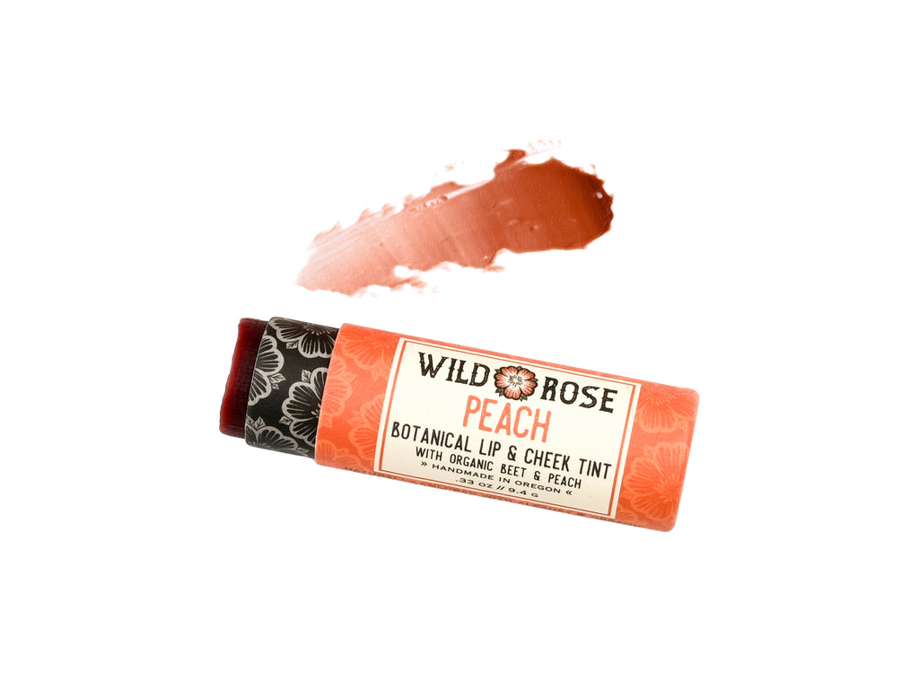 Wild Rose Peach Botanical Lip & Cheek Tint in a biodegradable paper tube on a white background. A color swatch is above, revealing a red-orange tint.