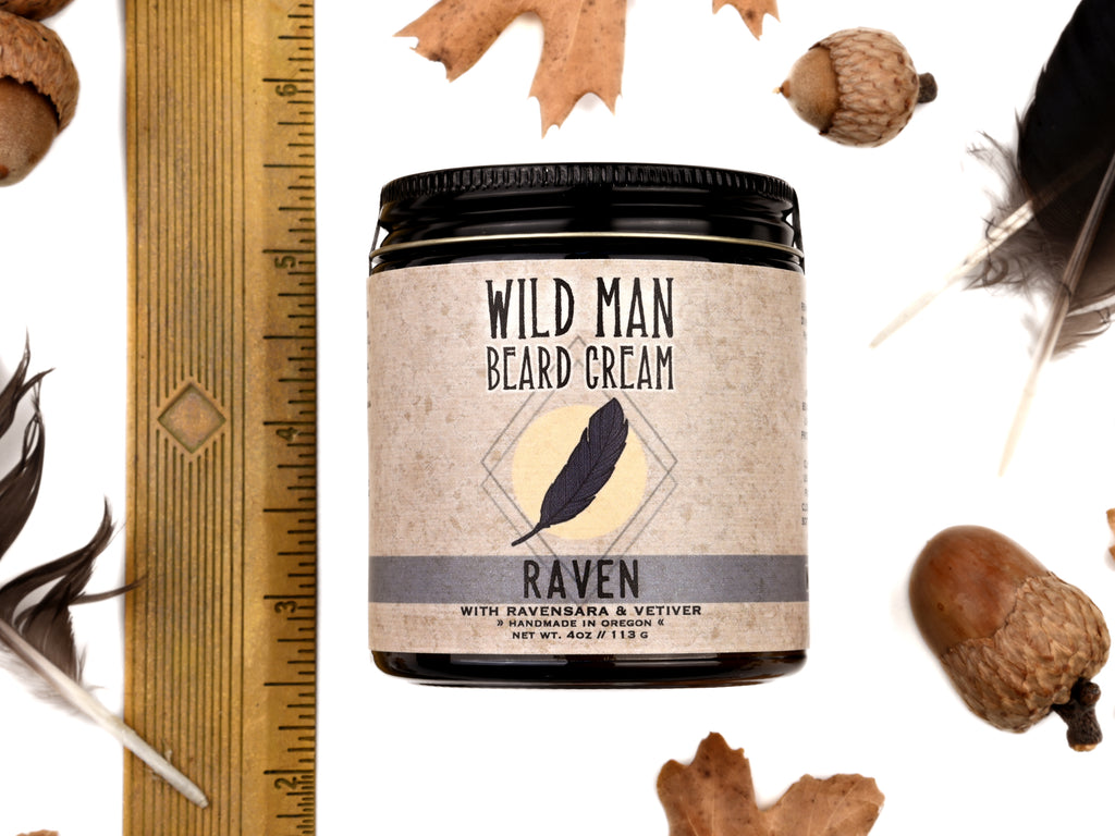 Wild Man Beard Cream - Raven scent in 4oz amber glass jar. Shown next to ruler at about 3" tall. Black feathers, acorns and dried oak leaves surround. 