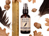 Wild Man Beard Wash - Raven scent in 2oz amber glass bottle. Shown next to ruler at about 5" tall. Black feathers, acorns and dried oak leaves surround. 