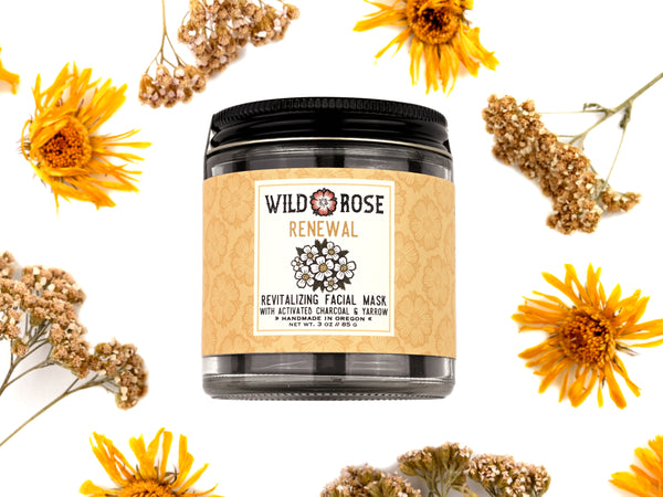 Wild Rose Renewal facial mask jar surrounded by yellow flowers and dried herbs on a white background