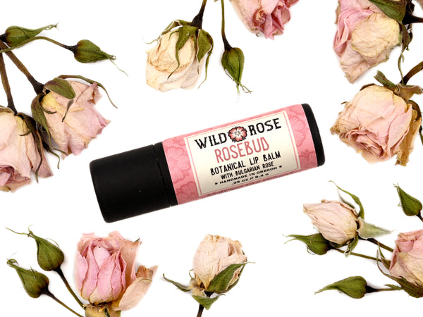 Rosebud Natural Lip Balm in a biodegradable paper tube. Dried roses surround.