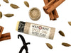 Wild Rose Spiced Chai Lip Balm in a biodegradable tube on a white background with cinnamon sticks, cardamom pods and vanilla bean. The cap is off revealing a creamy white balm.