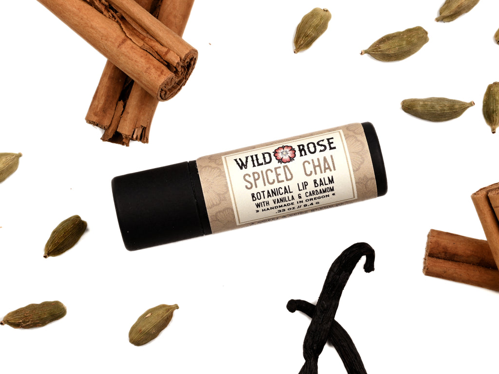 Spiced Chai Natural Lip Balm in a biodegradable paper tube. Cinnamon stick, cardamom and vanilla pods surround.