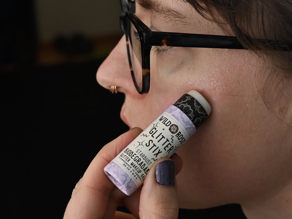 Person applying biodegradable glitter stix in Stardust to face with blurred background