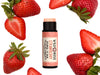 Strawberry Natural Lip Balm in a biodegradable paper tube with cap off revealing a naturally pigmented creamy pink balm. Fresh strawberries surround.