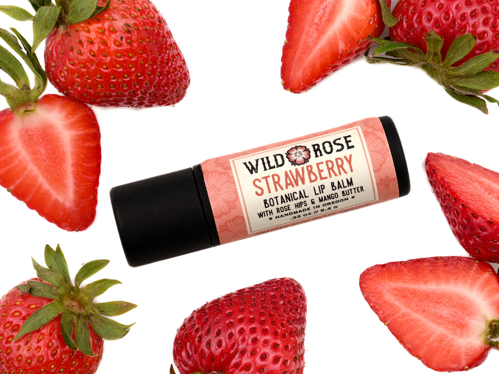 Strawberry Natural Lip Balm in a biodegradable paper tube. Fresh strawberries surround.