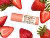 Wild Rose Strawberry Botanical Lip Balm in a biodegradable tube on a white background with fresh strawberries surrounding. 
