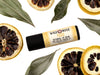 Yuzu Lip Balm in a biodegradable paper tube. Dried lemon slices and leaves surround.