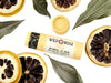 Yuzu Lip Balm in a biodegradable paper tube. Dried lemon slices and leaves surround.