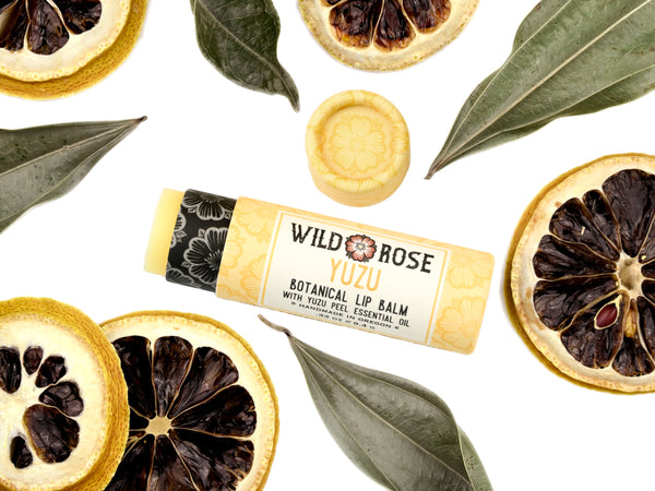 Yuzu Lip Balm in a biodegradable paper tube. Dried lemon slices and leaves surround.
