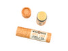 A tube of Wild Rose Apple Cider Botanical Lip Balm is displayed on a white background. The lip balm tube has a light orange label with black and orange text, a black patterned band, and a pale yellow balm stick visible.